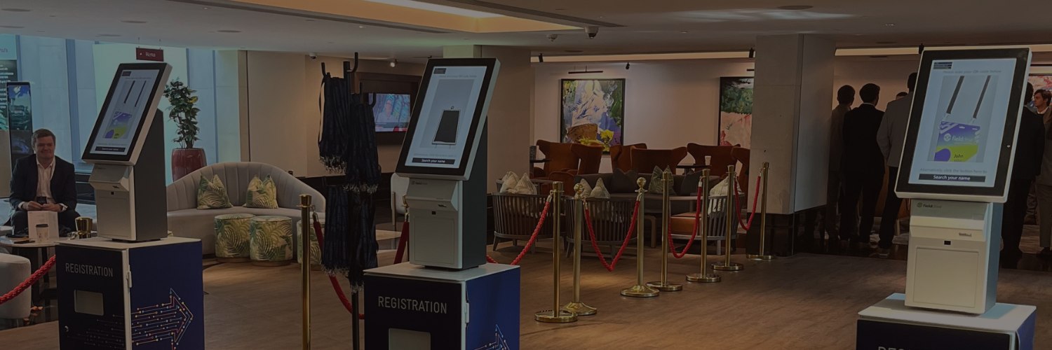 Event registration area featuring multiple touchscreen kiosks placed on branded stands with roped‑off queue lanes.