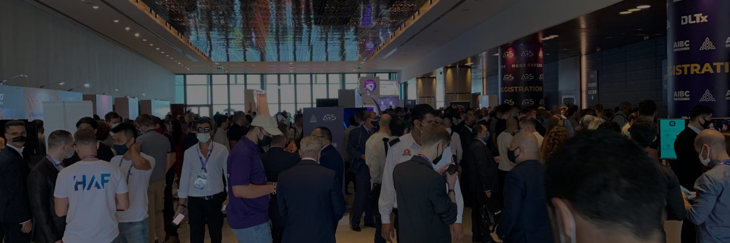 Busy conference hallway filled with attendees gathered near exhibition booths and registration signage.