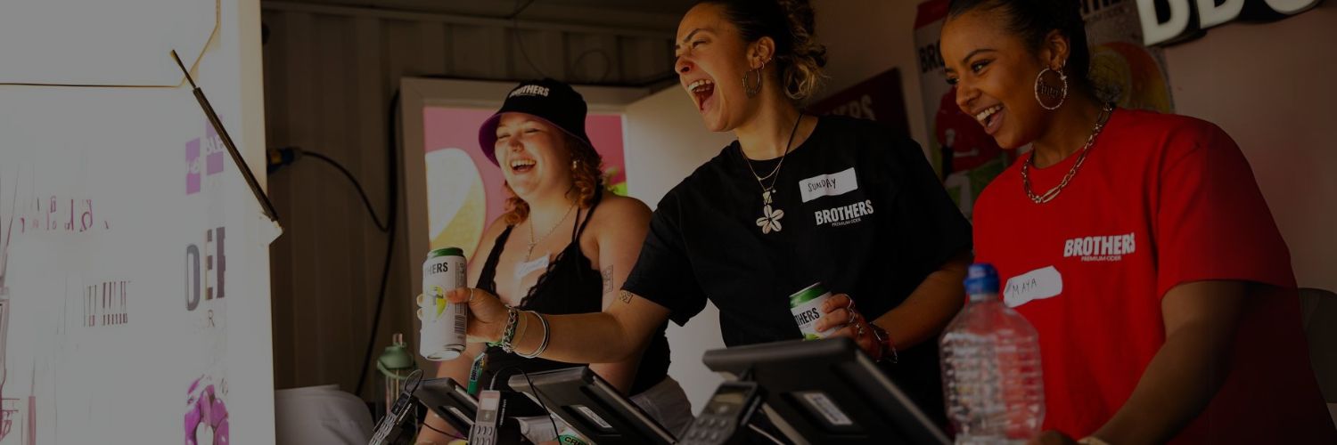 Event bar counter with staff operating multiple POS terminals and handing out canned drinks.
